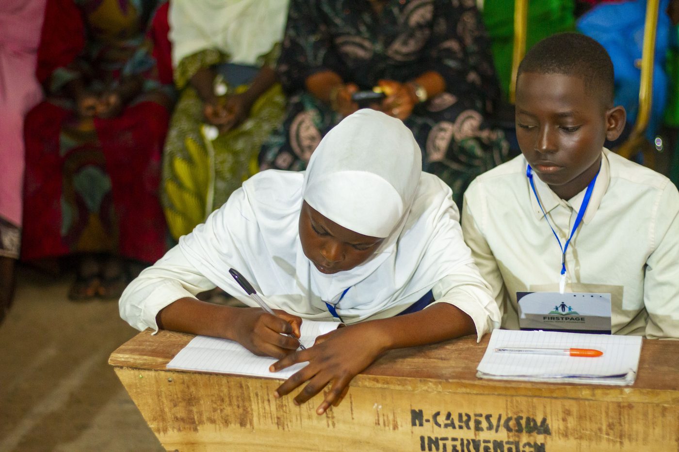A FirstPage Foundation student writing during an academic competition, seated beside a fellow participant