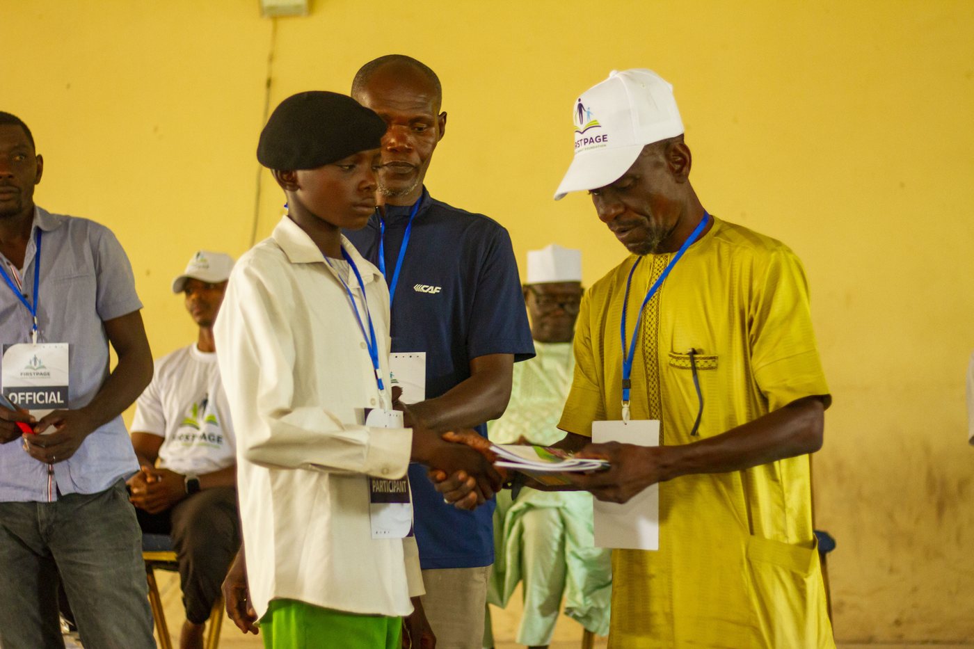 A FirstPage Foundation official presenting a certificate to a student participant with a handshake